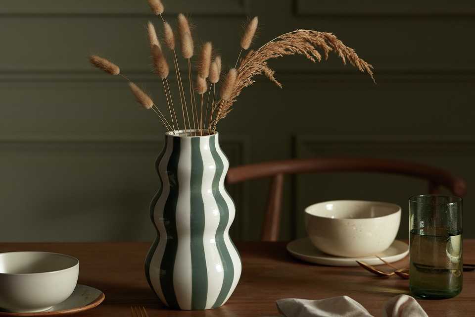 Habitat Hand Painted Stripe Vase in green colour placed on a wooden dining table.