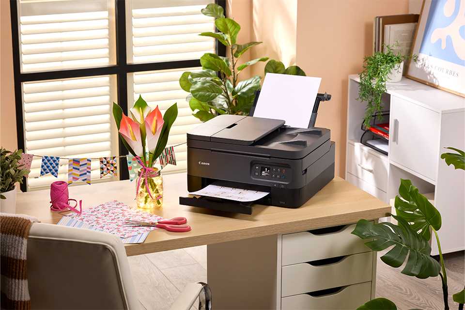 A Canon PIXMA TS7450A home printer with painting tools scattered on a table.