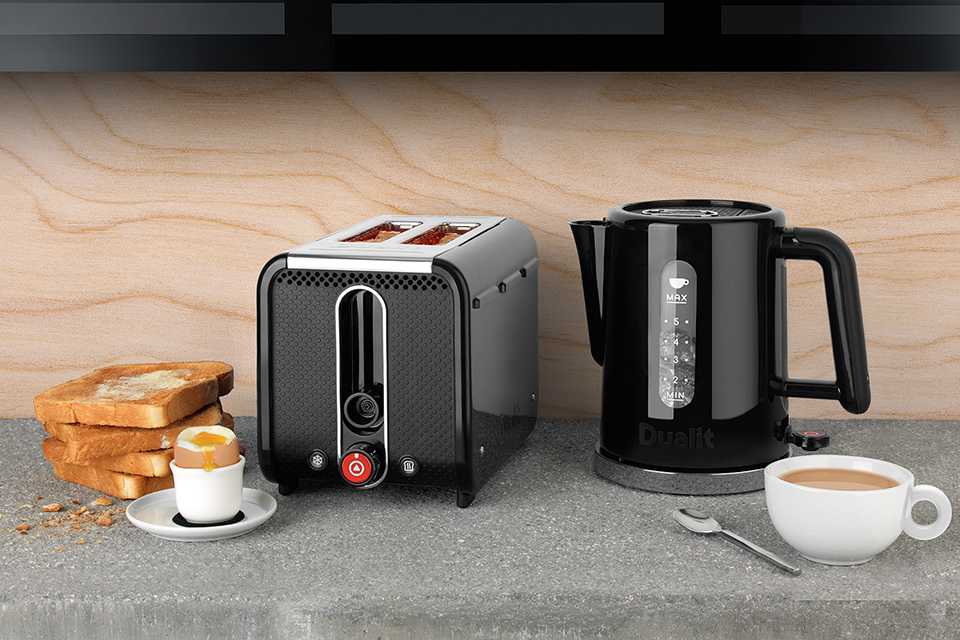 A black Dualit Studio kettle and a 2 slot toaster with cups of coffee and toasted bread next to it.