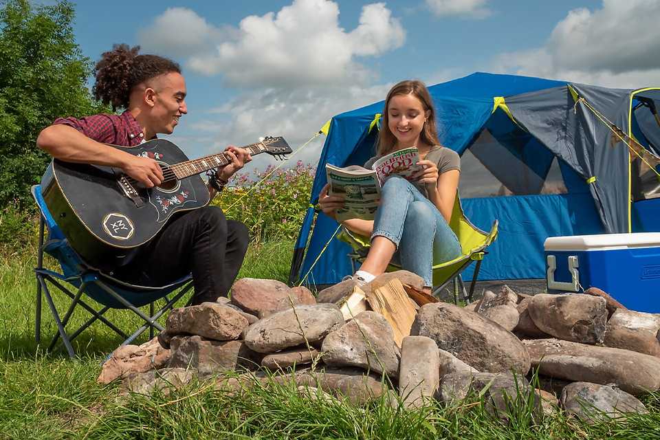two people sit by a camp fire with a tent in the background