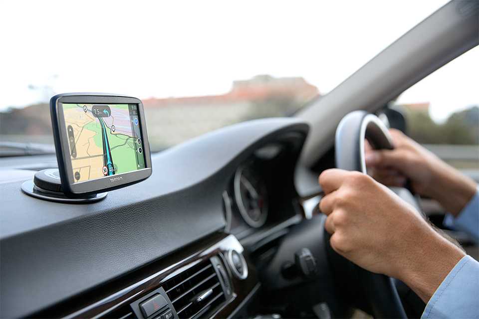 Close-up shot of a pair of hands driving and a Sat Nav installed in a car.