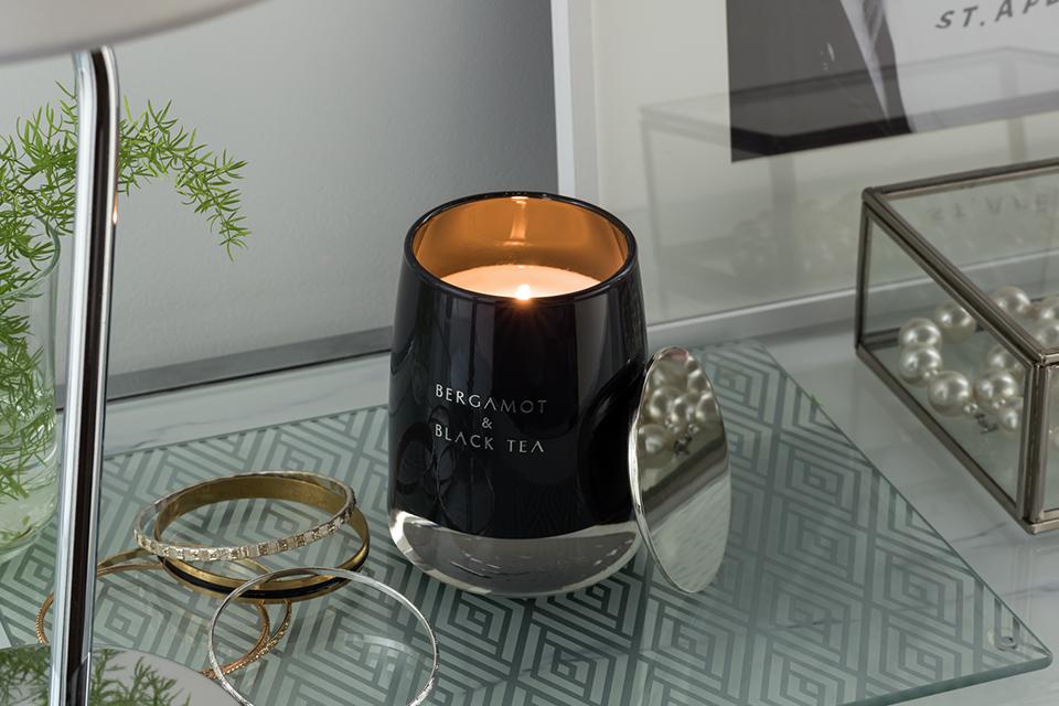 The Argos Home candle with lid in black on a table next to jewellery.