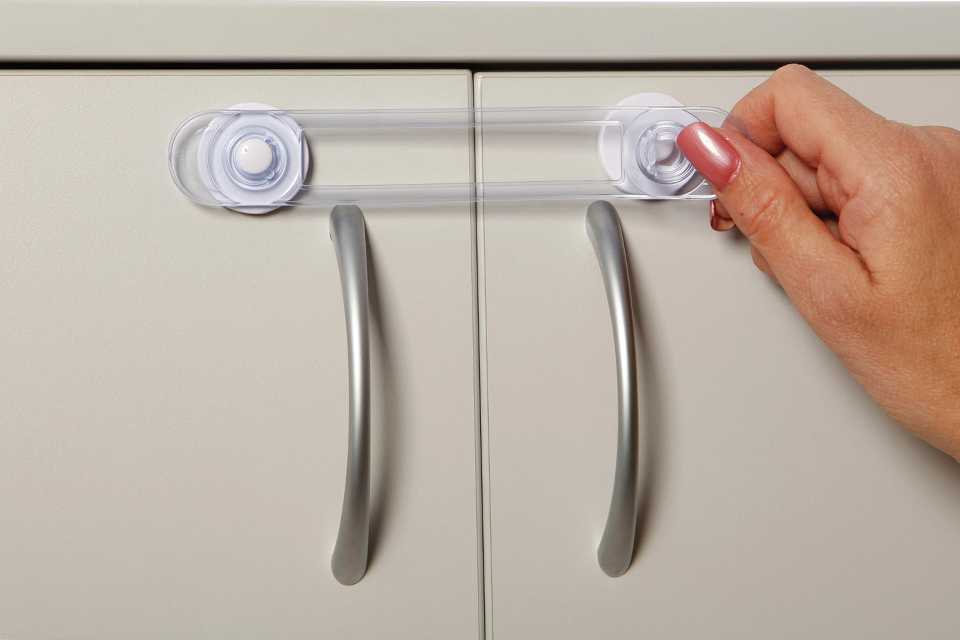 A woman's hand securing Dreambaby safety lock on a cabinet.