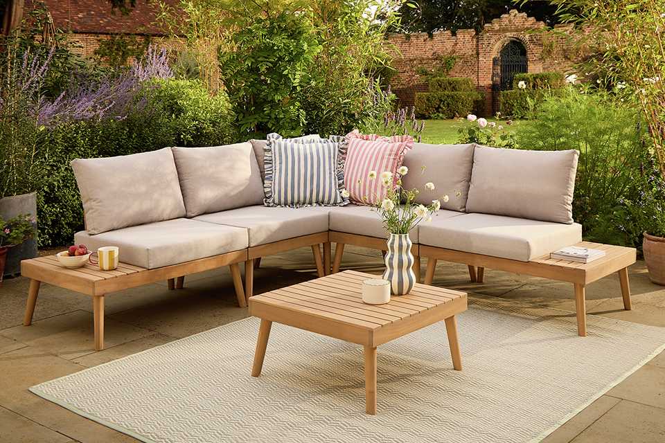 A Habitat wooden outdoor sofa with striped cushions placed outdoors paired with a wooden coffee table and beige outdoor rug.