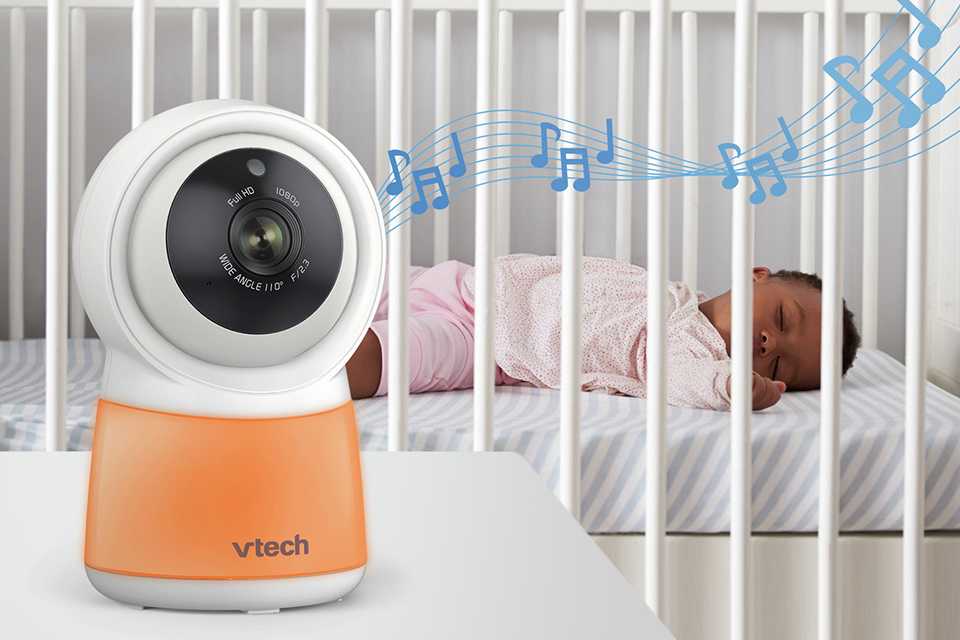 A VTech RM5755 5inch HD Smart Video Baby Monitor next to a baby in a cot bed.
