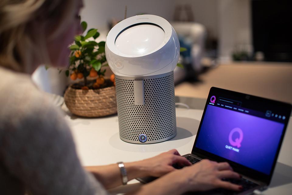 Lady on laptop looking at Quiet Mark website, with a Dyson pure cool me fan next to her.