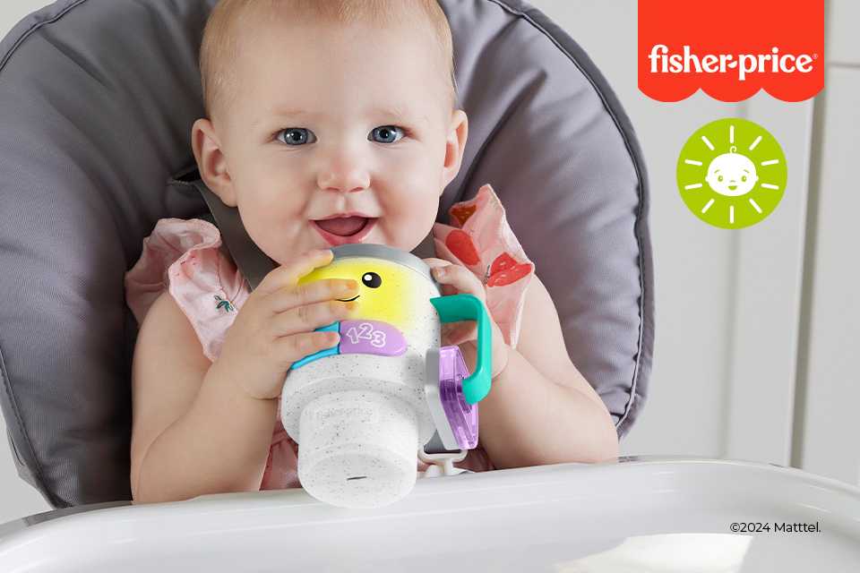 A baby holding a Fisher-Price sipper while smiling at the camera.