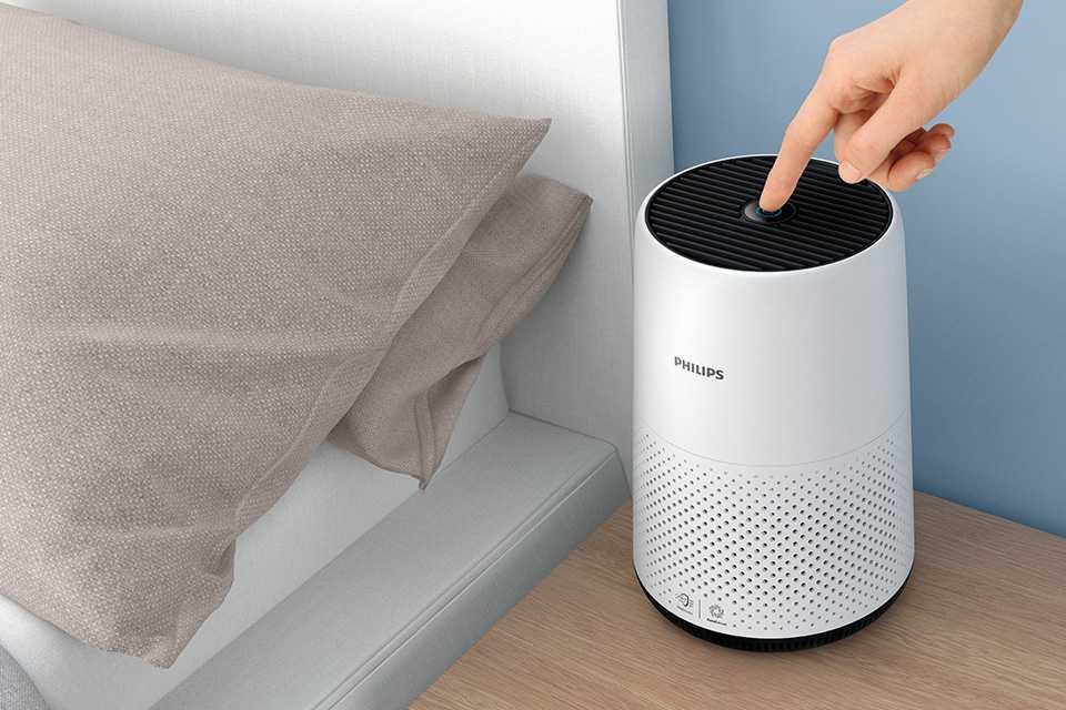 A finger switching on a white Philips 800 Series Air Purifier placed on a beside table.
