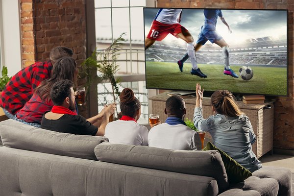 A group of friends watching a football game on a TV sitting on a sofa.