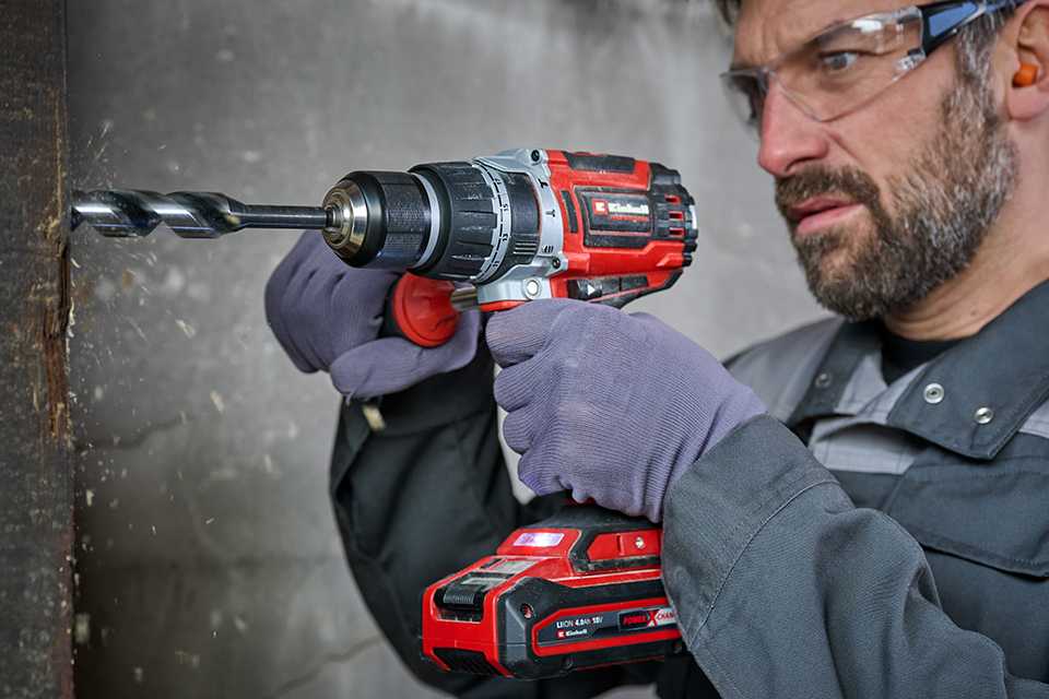 A man using Einhell red and black cordless drill against concrete.