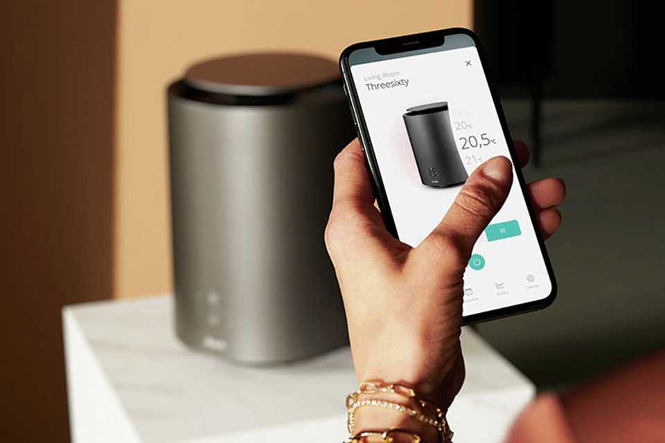 A woman setting the Duux ThreeSixty Smart Ceramic Fan Heater on her phone.