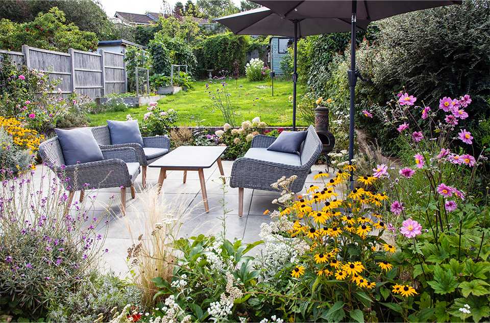 A beautifully set up garden with garden furniture, plants and trees on a bright, summer day.