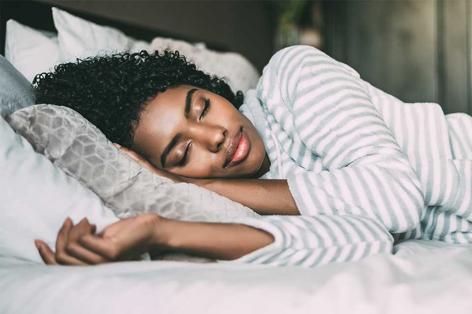 A woman sleeping on a bed with grey and white bedding.