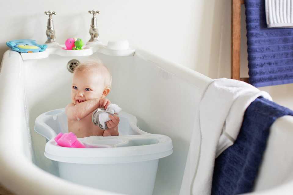A baby having fun while bathing in the baby bath tub placed in a large bath tub.