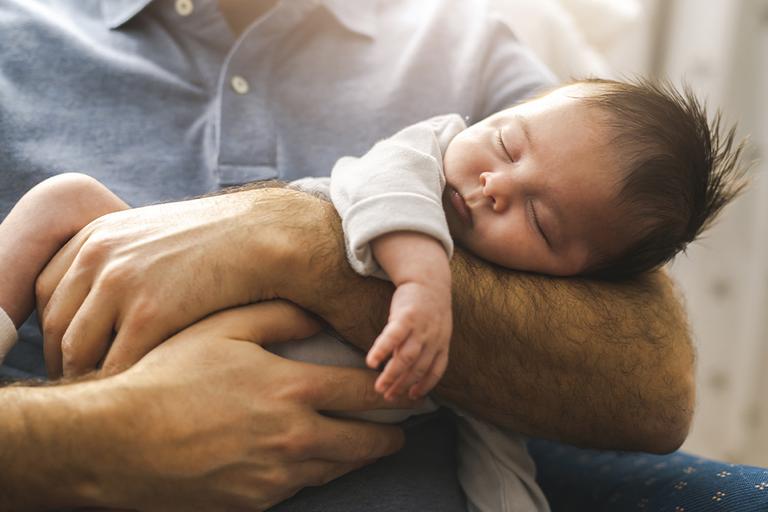 A new born baby sleeping in their father's arms.