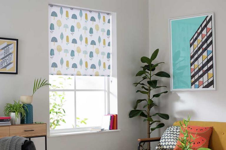 A Habitat multi-coloured, daylight trees roller blind on a window.