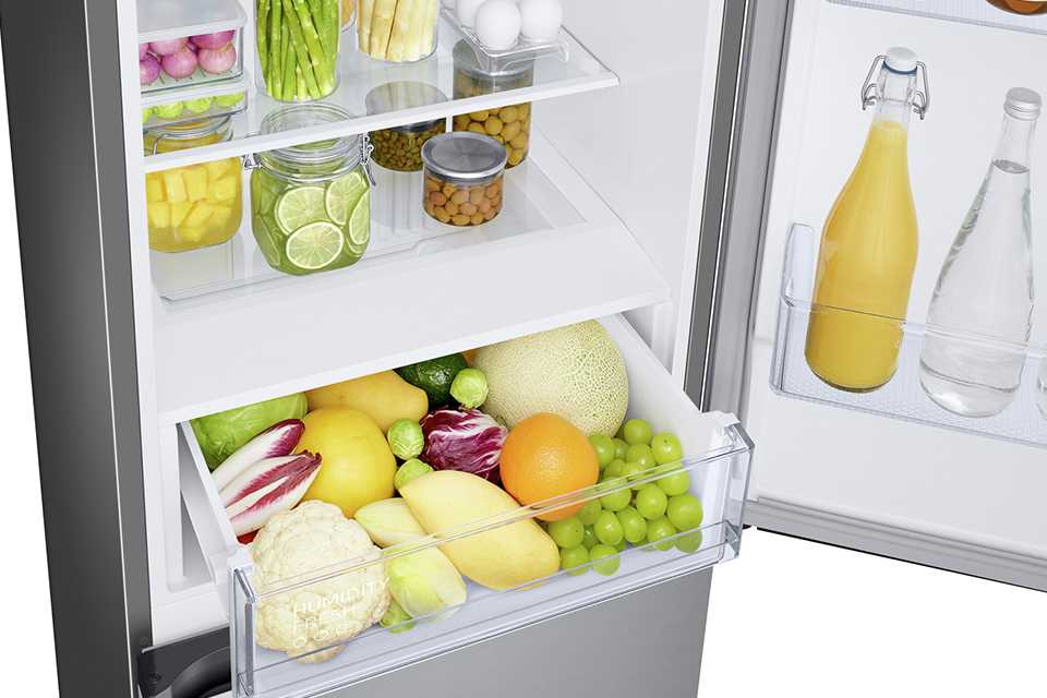 Fresh fruits and vegetables along with bottles stored in the door and shelves of a Samsung freestanding fridge freezer.