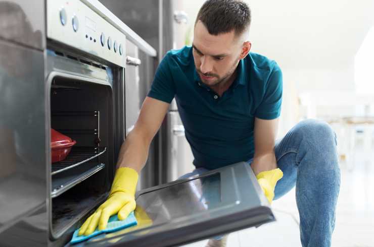 A man wiping the oven door with a cloth.