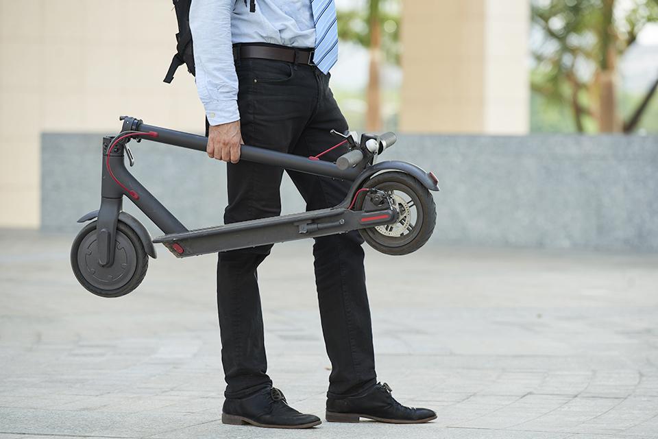 Business man carrying a folded electric scooter.
