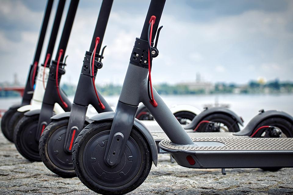 Four black electric scooters lined up on pavement.