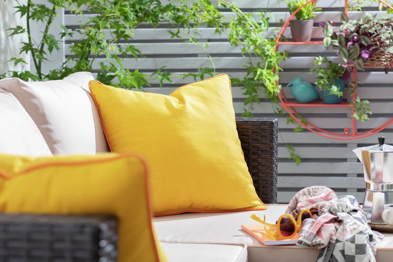 Rattan garden chair with cream and yellow cushions in garden.