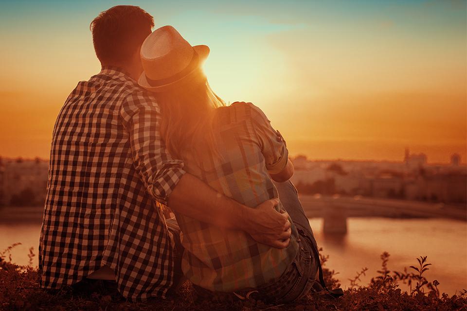 A couple embracing while sitting and watching the sun setting.