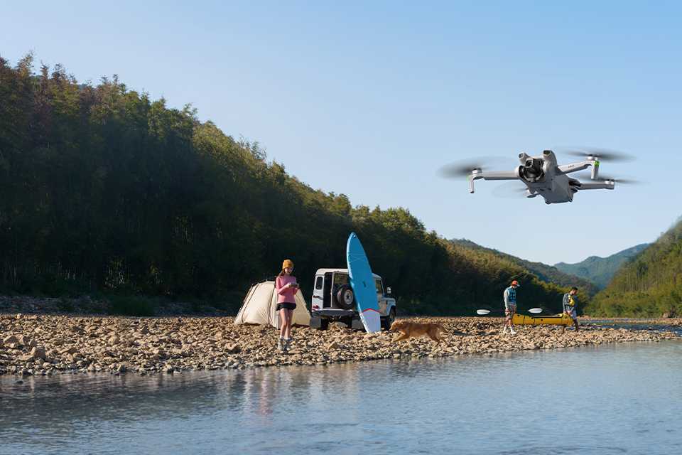 A woman flying a DJI Mini 3 camera drone at a beach.