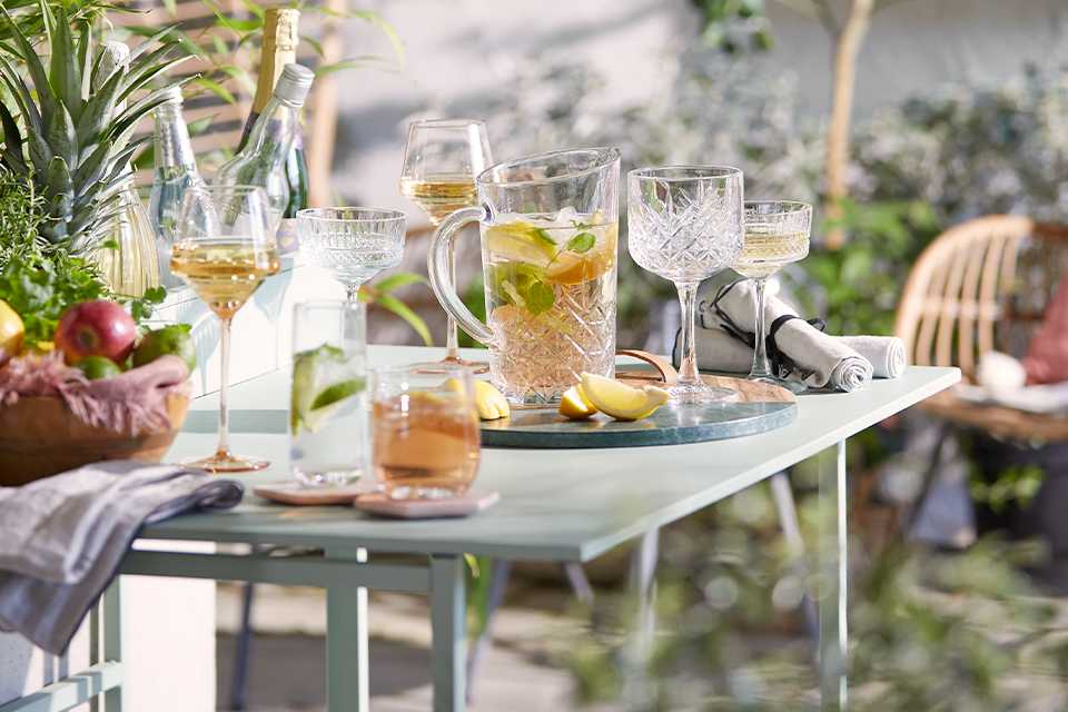 A table full of glasses, a jug of cocktail and a fruit bowl.