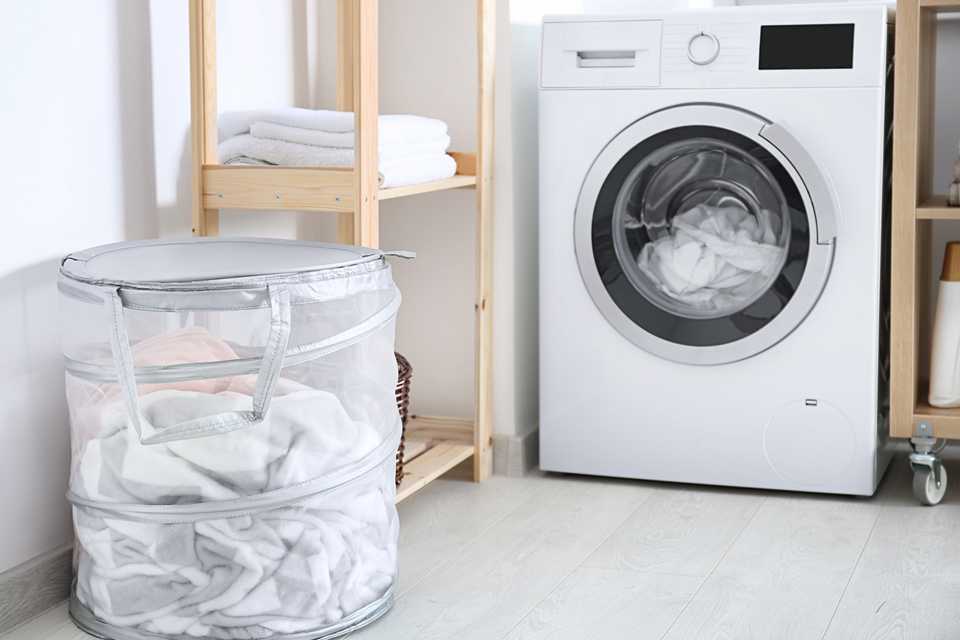 A white washing machine in a utility room next to a wooden storage rack and white laundry basket.