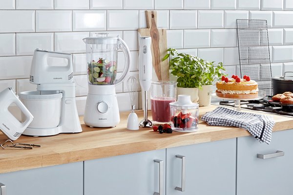 A white Cookworks stand mixer, hand blender and a jug blender on a counter with other food items.