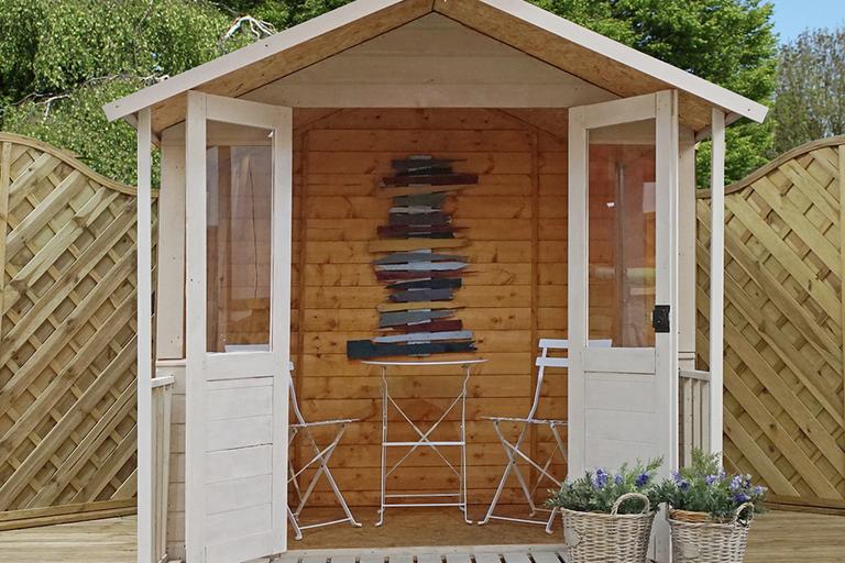 Wooden summer house in garden, with table and chairs inside.