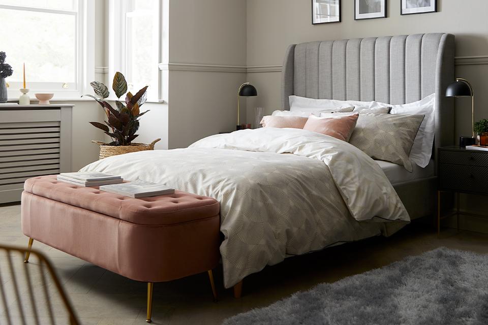 Grey high headboard bed with pink ottoman storage.