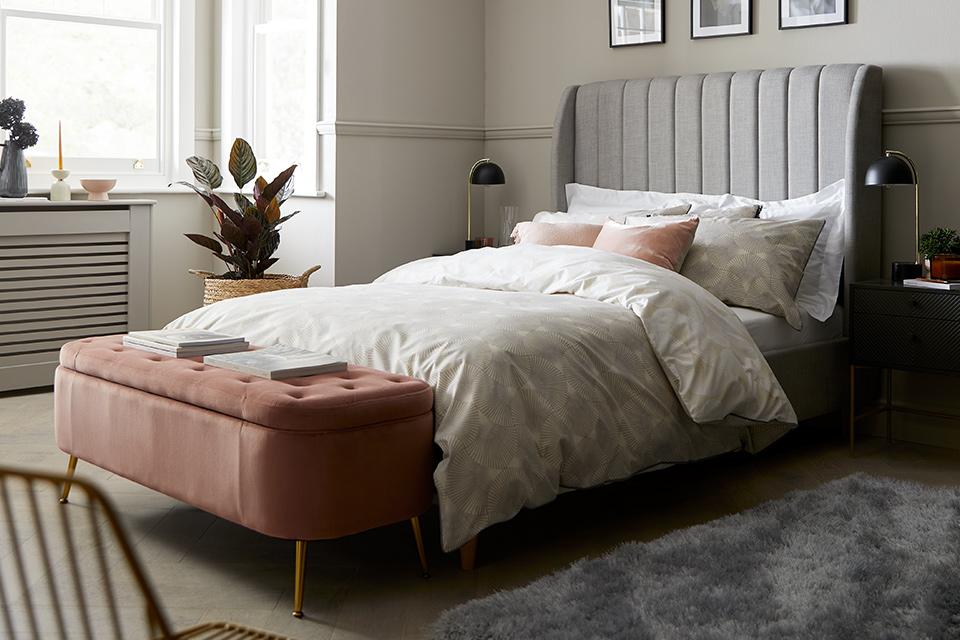 Grey high headboard bed with pink ottoman storage.