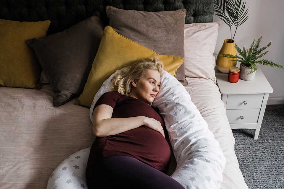 A pregnant woman using a pregnancy pillow to sleep on the bed.