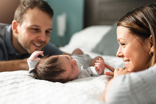 A happy couple smiling while looking at their newborn baby on the bed.