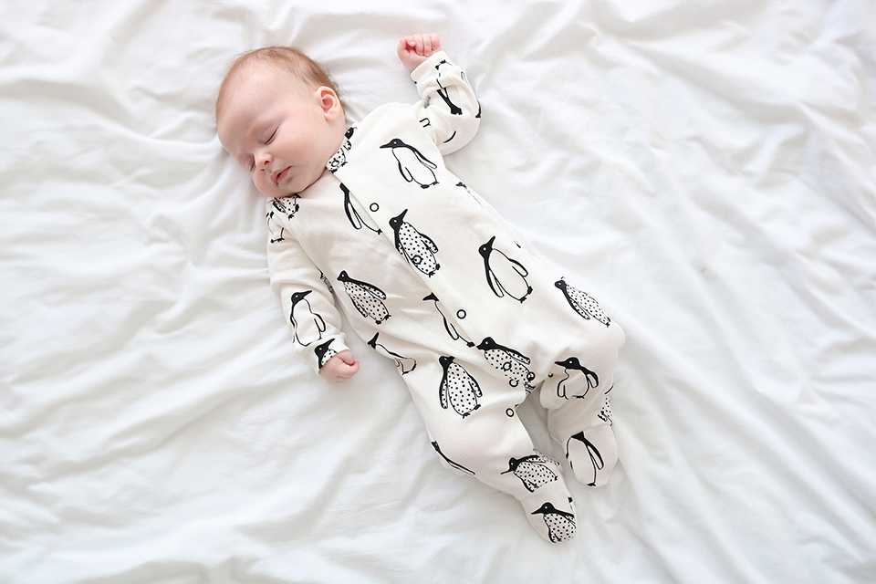 A baby sleeping in a penguin printed sleepsuit.