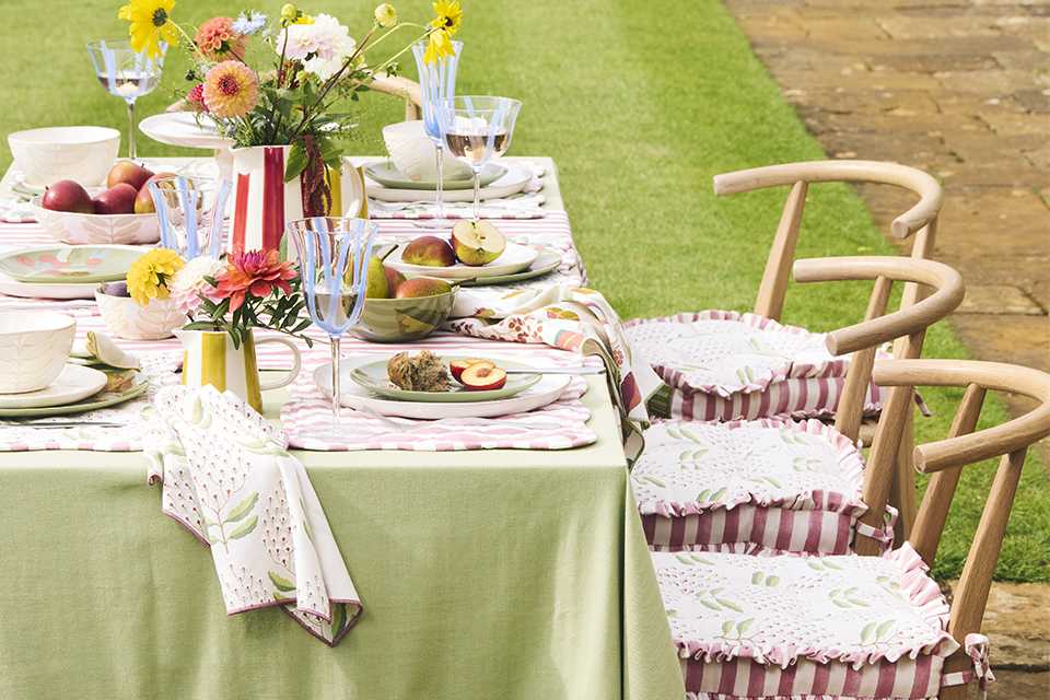 A table set outdoors with National Trust products like elegant glasses, tableware, and seat cushions.