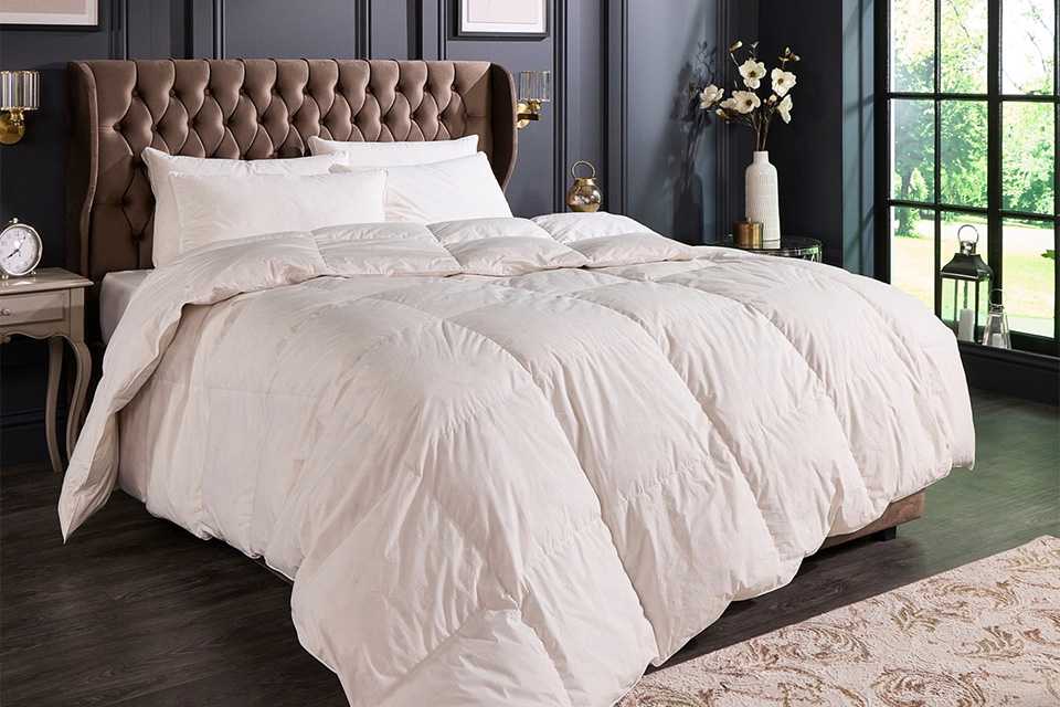 A bed made with a Hungarian goose feather duvet and two pillows next to some flowers and a window.