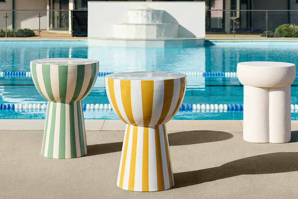 A Habitat side table in white and two side tables with bright yellow, and green stripes next to a pool.