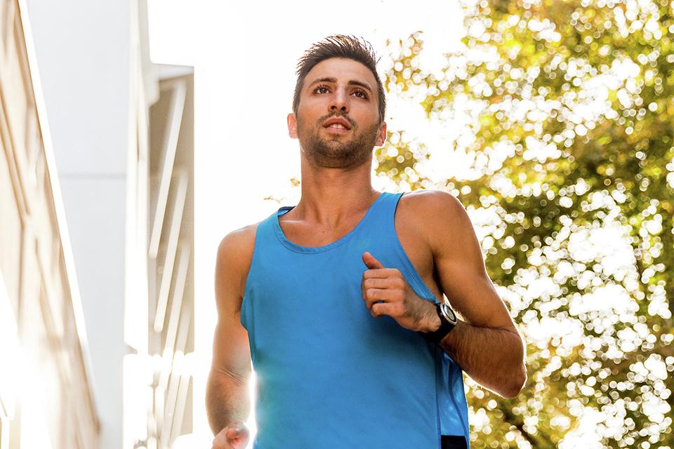 A man running outside in sunny weather with a blue vest and black shorts on.