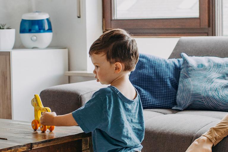 A young boy plays with toys in a living room, a Vicks humidifier can be seen in the background.