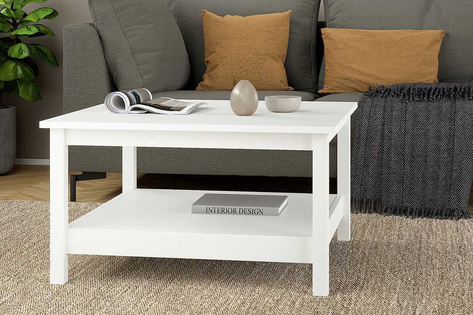 A Tvilum Madrid white coffee table placed in front of a white sofa in a living room.