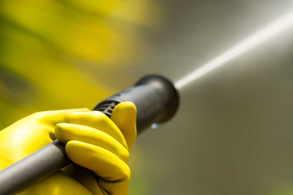 A person using a pressure washer wearing yellow rubber gloves.