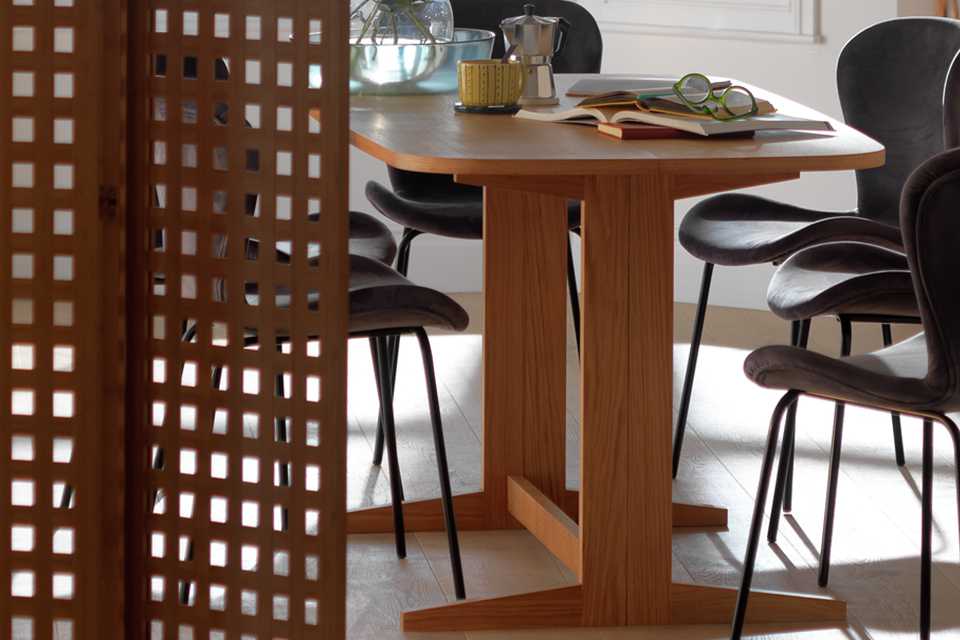 Dining room with wooden table, grey velvet chairs and a room dividing wooden screen.