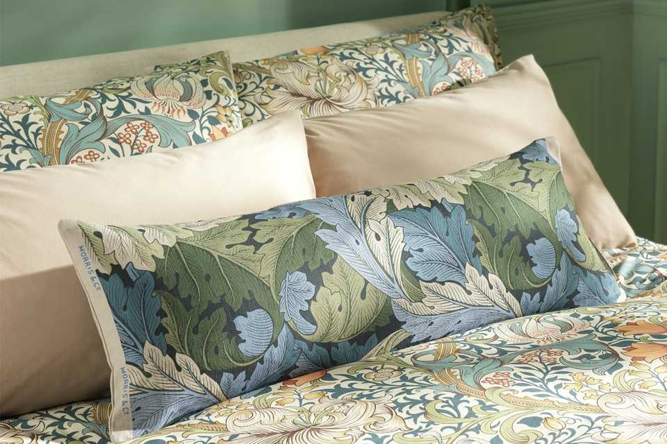 Habitat x Morris & Co. Acanthus Bolster Cushion in blue colour placed on a green bed.