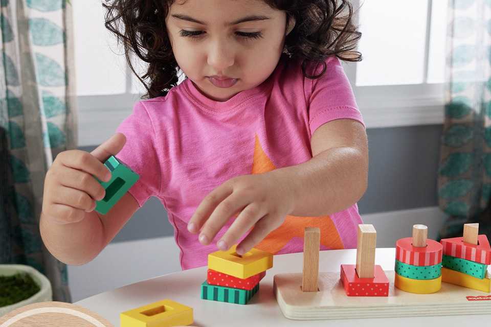 A child playing with a Fisher-Price Wooden Shape Stacker Toddler Sorting toy.