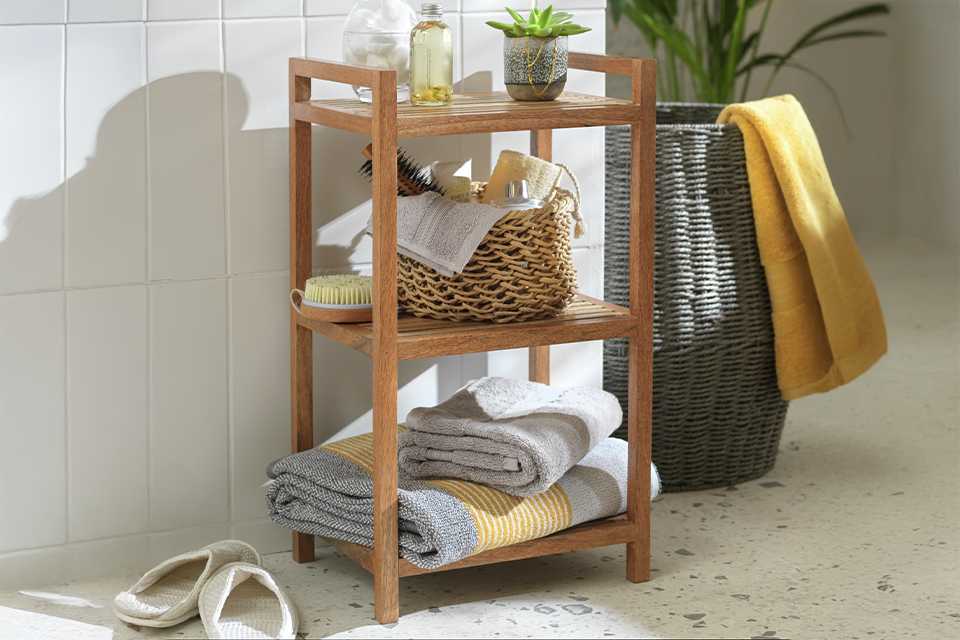 A Habitat Mango Wood Bathroom Storage Shelf Unit with a storage basket and some towels.