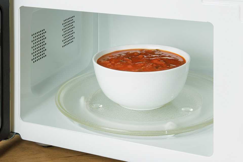 A white bowl of curry placed inside a white microwave.
