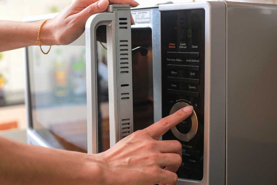 A woman pressing a button on a microwave while closing its door ready to use.