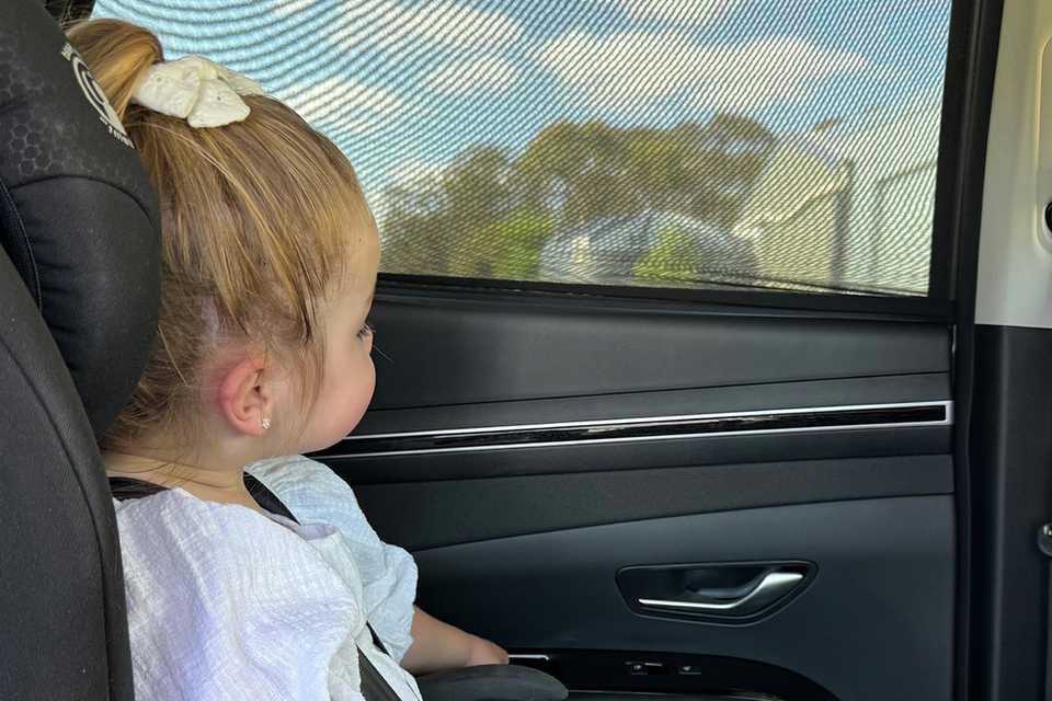 A girl looking out through a Dreambaby Car Window Shade/Socks.
